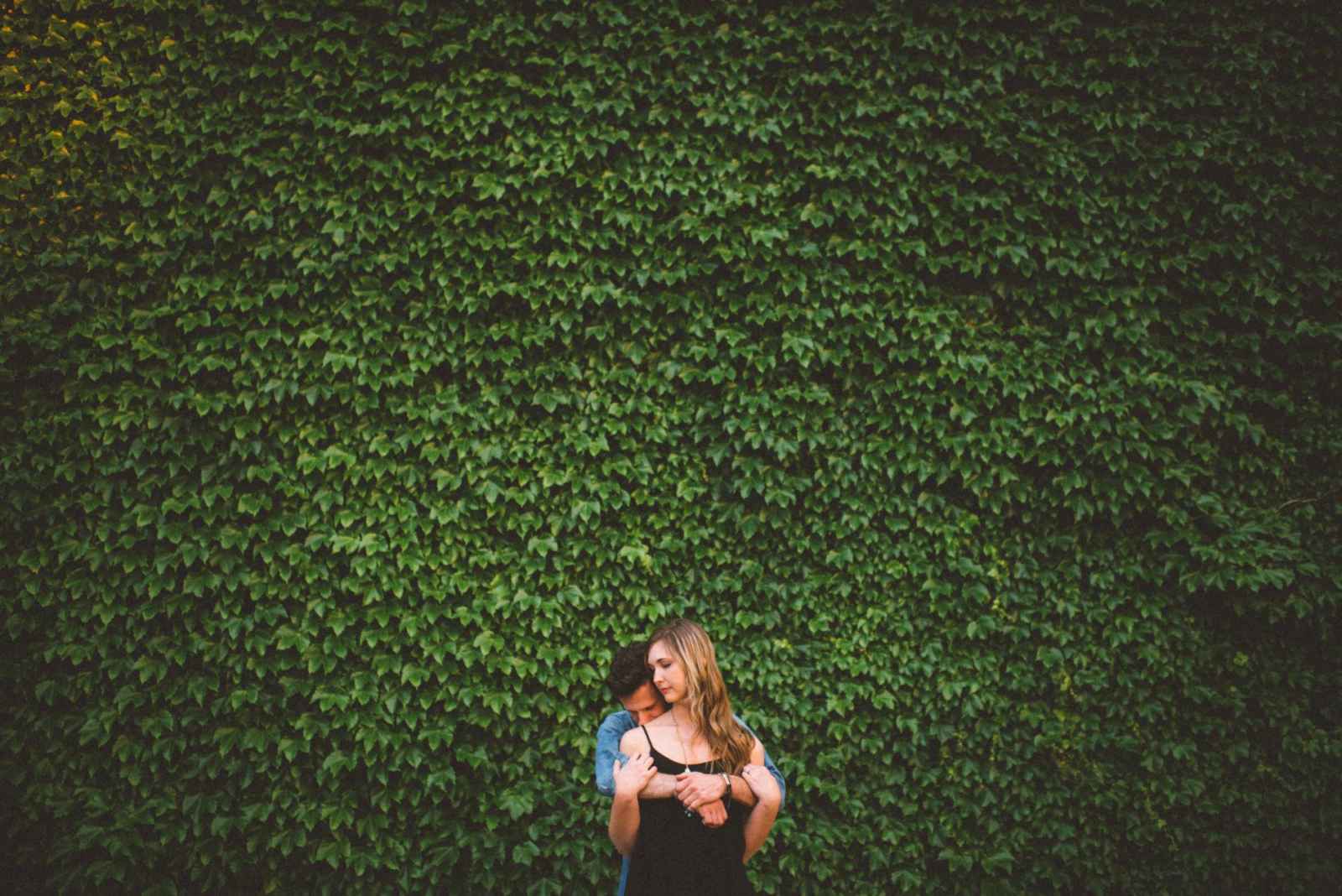 couple posing in front of grass wall