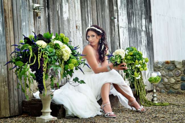 Bride Sitting by Large Centerpieces of Lush Greenery