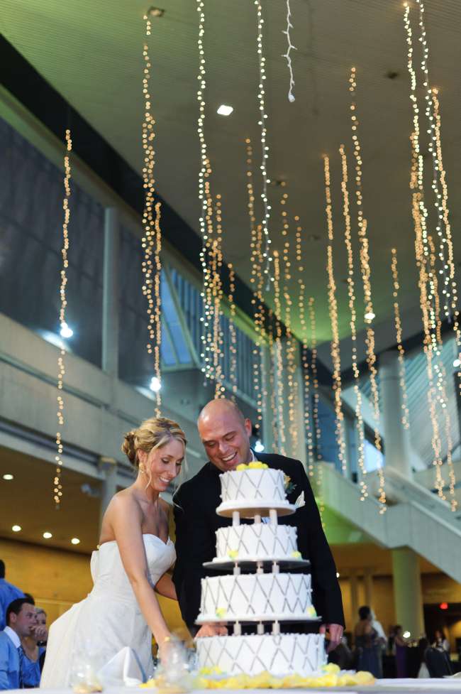 Bride & Groom Cutting Cake in Front of Elegant String Lights